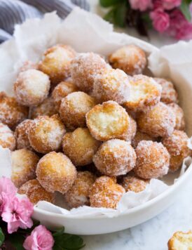 Homemade donuts in a serving bowl. Two are bitten into to show texture of interior.