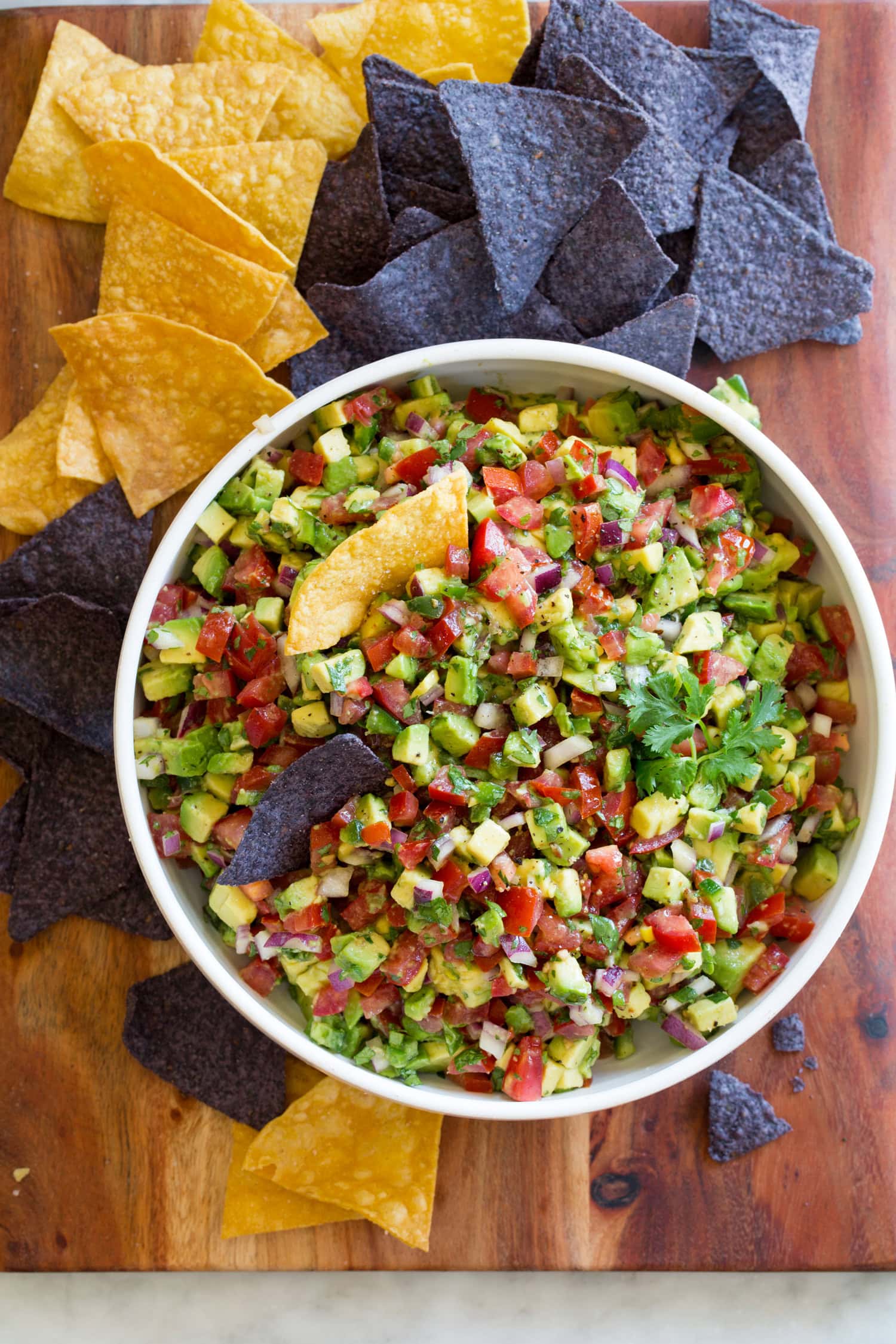 Avocado salsa in a bowl with yellow and blue tortilla chips to the side.