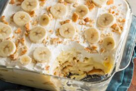 Banana pudding in glass square dish with scoop removed to show layers of the dessert.