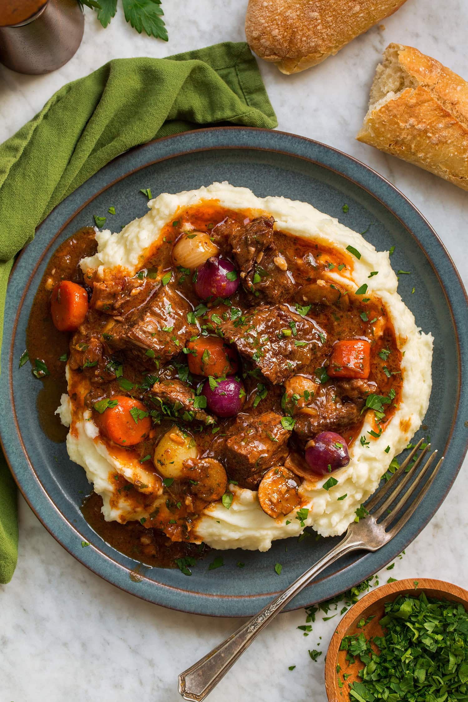 Beef bourguignon with potatoes served on a blue plate with a green napkin cloth to the side.