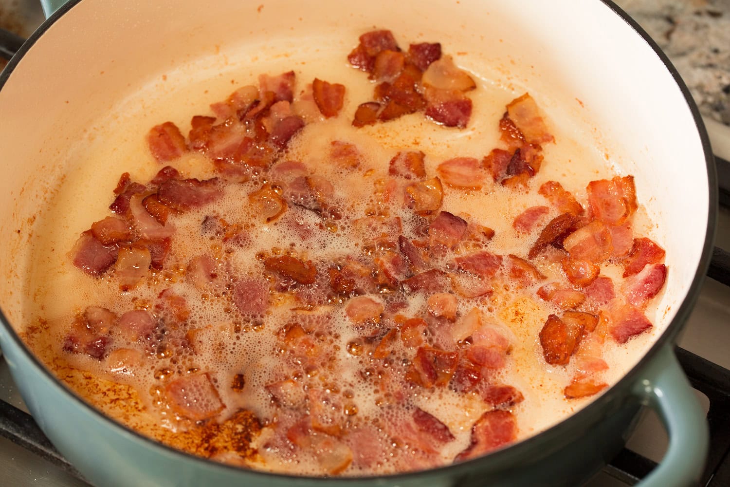 Bacon pieces cooking in a pot.