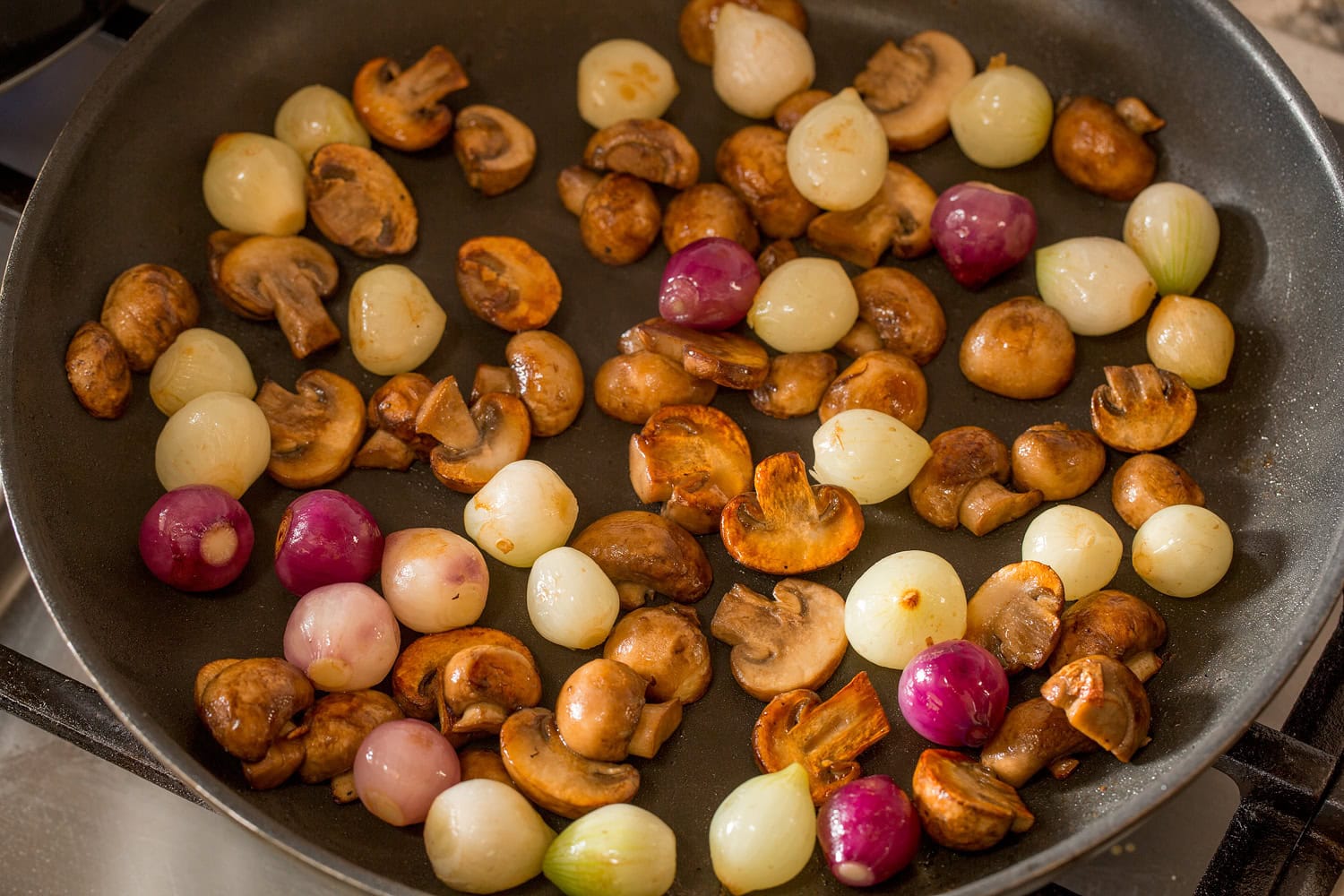 Mushrooms and pearl onions being sauteed in a skillet.