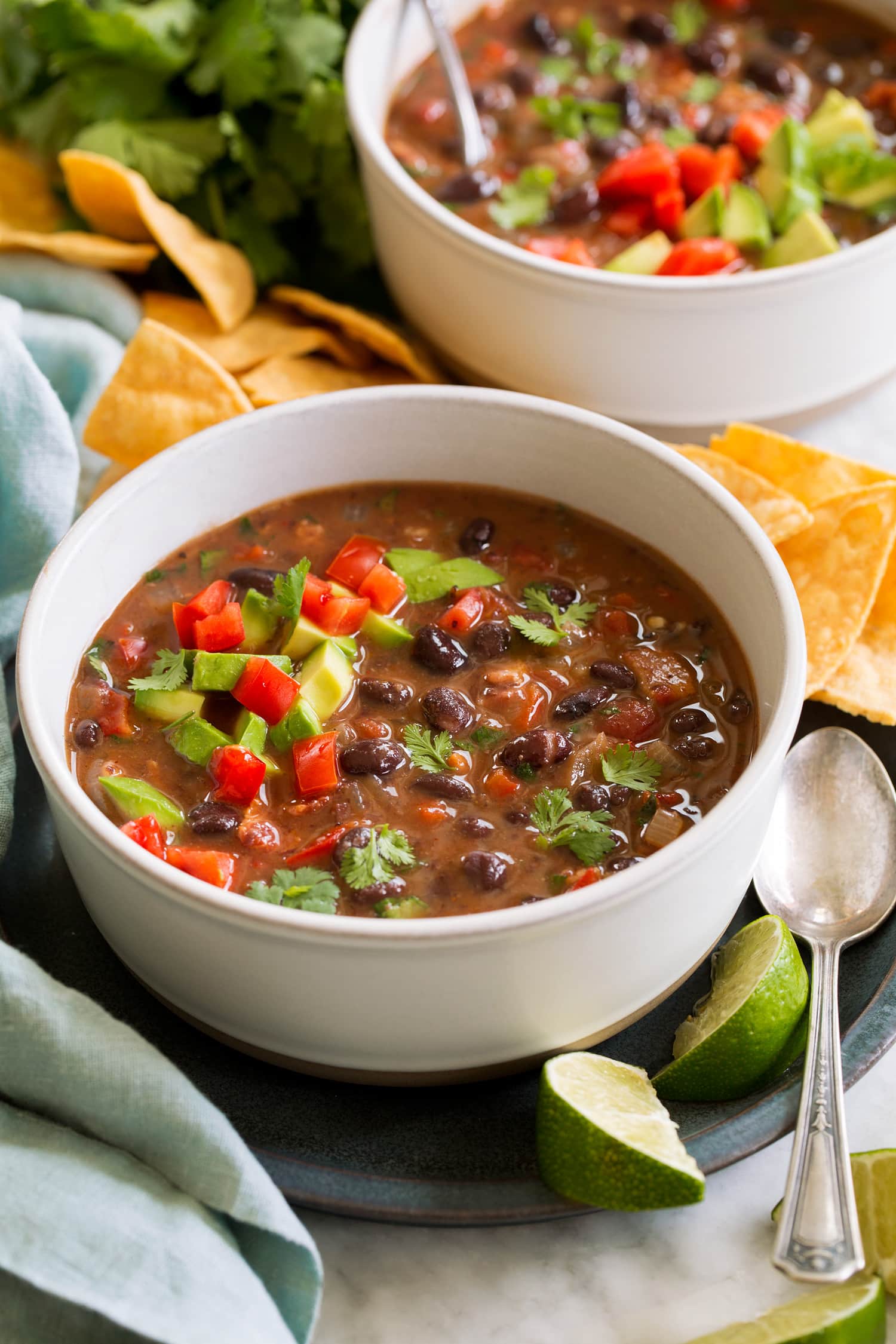 Serving of homemade black bean soup topped with tomatoes, avocado and cilantro.