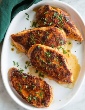 Row of blackened chicken breast on a white oval platter over a marble surface with a green cloth to the side.