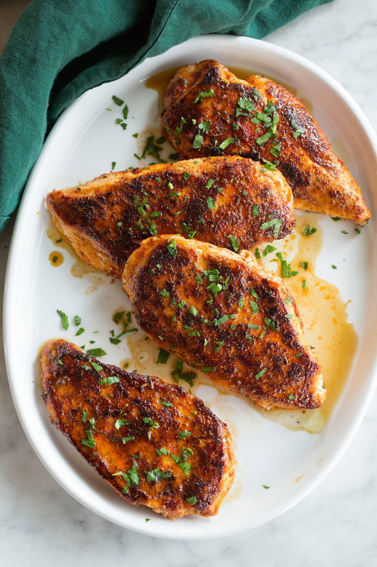 Row of blackened chicken breast on a white oval platter over a marble surface with a green cloth to the side.