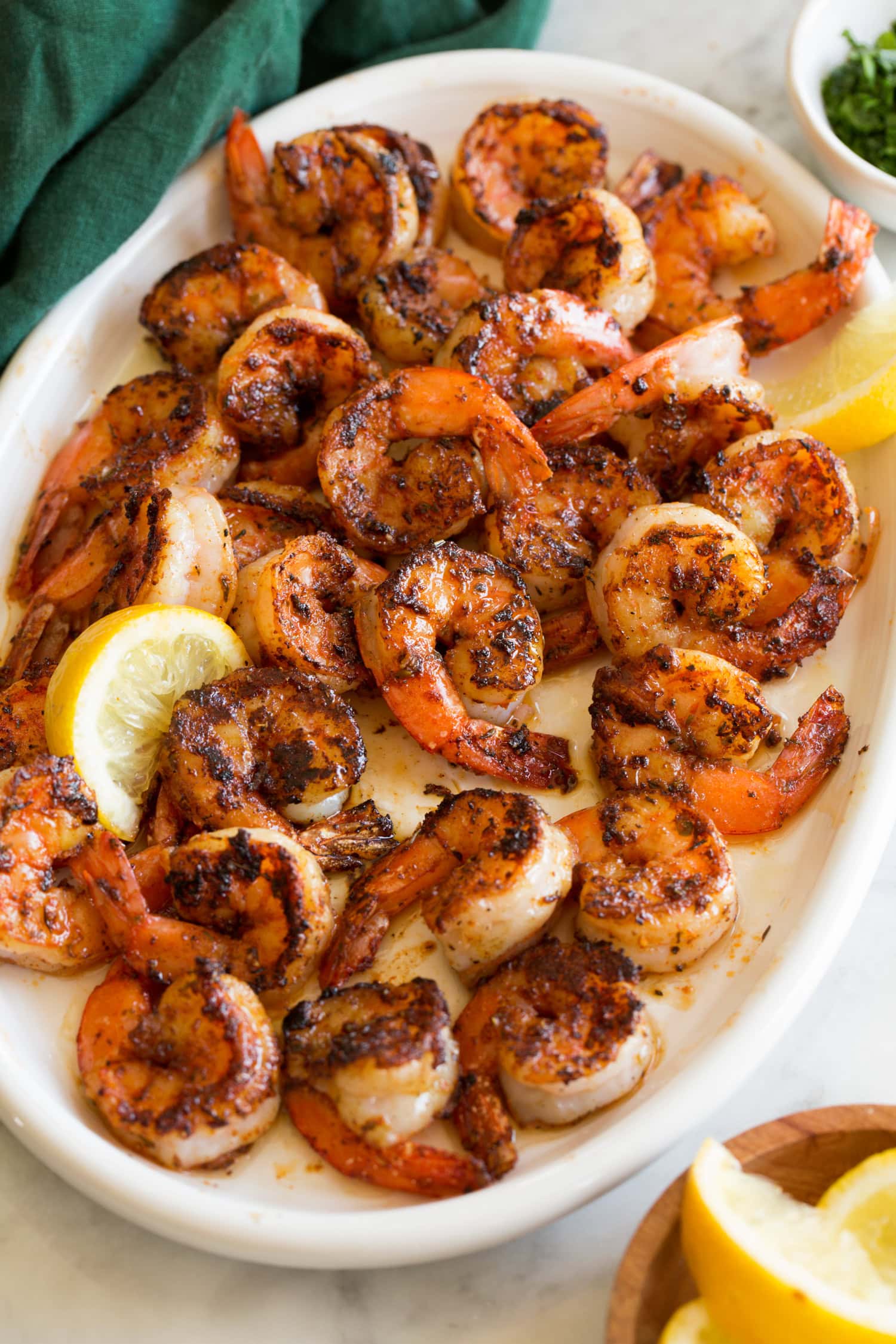 Seasoned blackened shrimp on a white serving platter with a green cloth to the side.