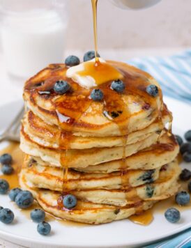 Pouring syrup over stack of homemade blueberry pancakes