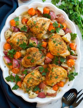 Braised chicken and vegetables on a white oval platter on a marble surface..