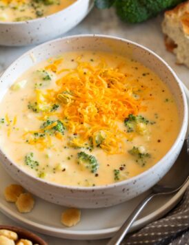 Single serving of broccoli cheese soup in a white bowl with crackers to the side.