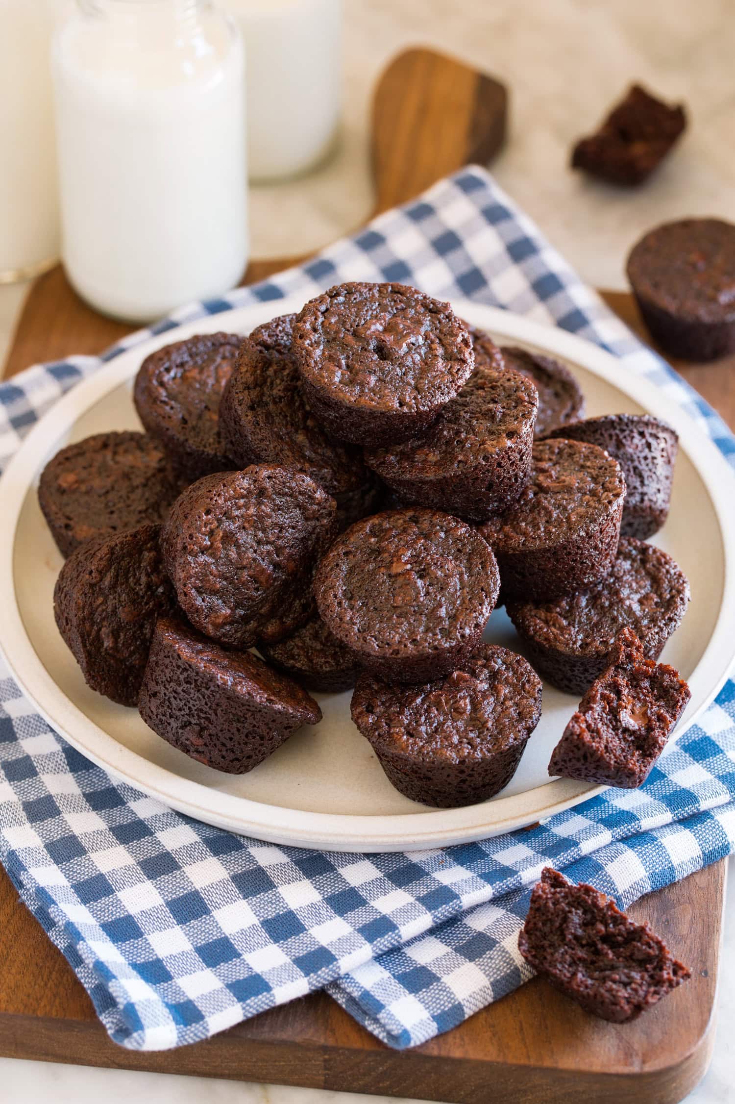 Homemade brownie bites stacked together on a plate over a blue checkered napkin.