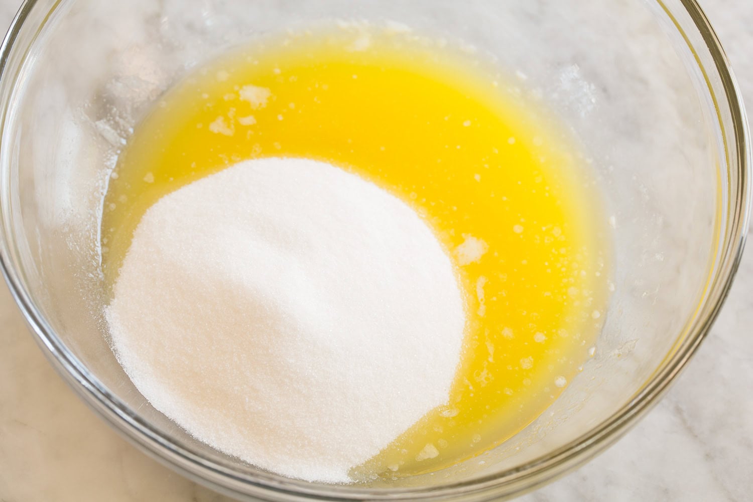 Melted butter with white sugar in a glass mixing bowl.