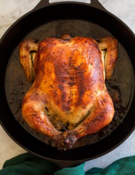 Whole brined and roast chicken shown overhead in a cast iron skillet.