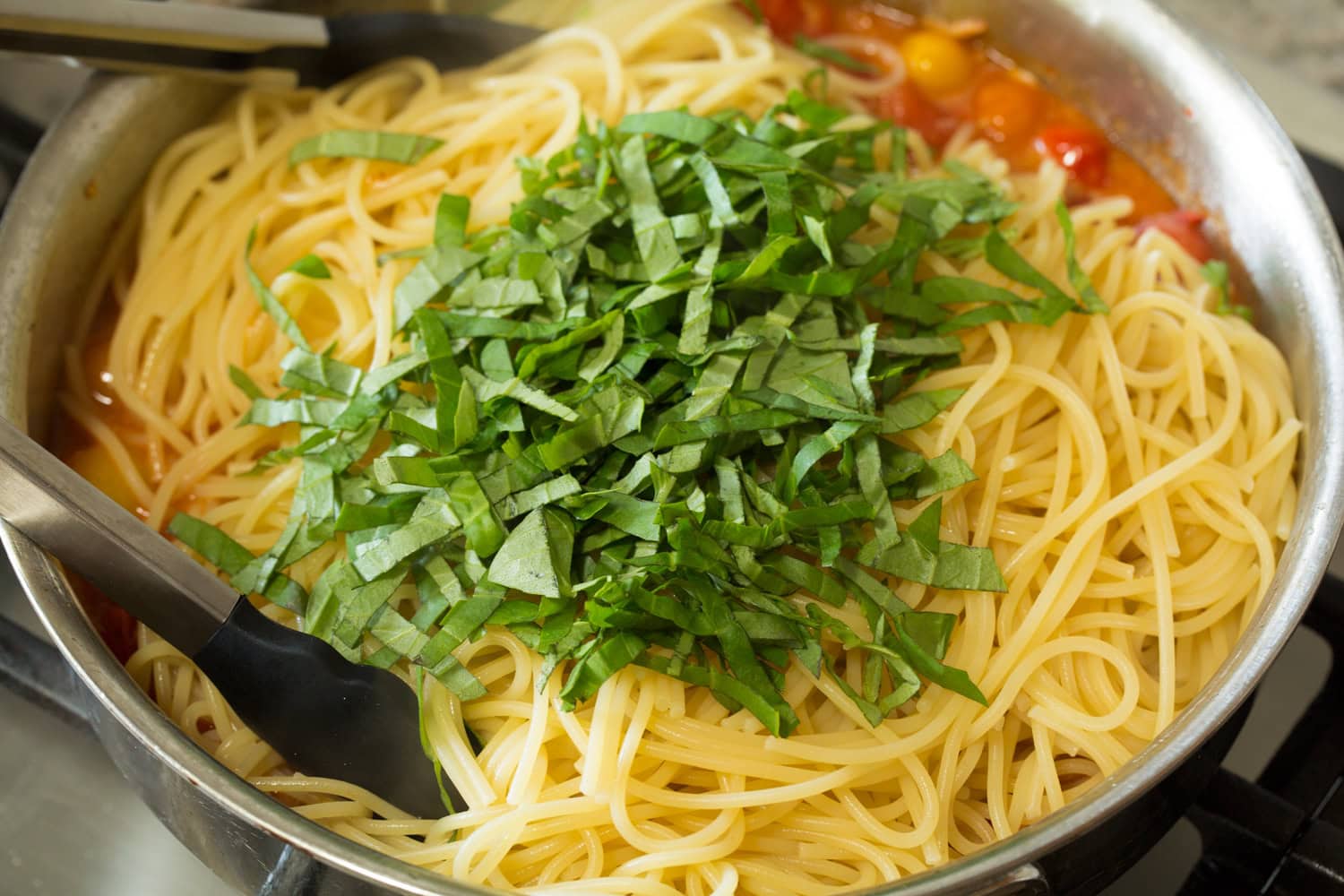 Basil and pasta being added to sauce.