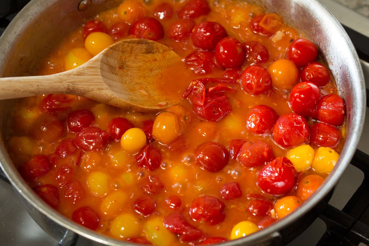 Smashing cherry tomatoes into sauce in saute pan.