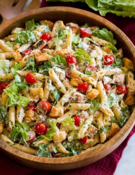 Side angle shown of chicken caesar pasta salad with romaine lettuce, chicken, croutons, parmesan and tomatoes.