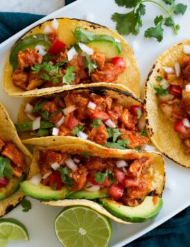 Chicken tinga tacos lined up on a serving plate.