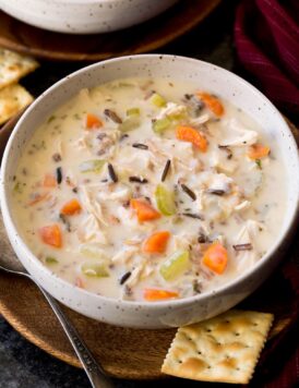 Serving of chicken and wild rice soup shown in a white bowl over a wooden plate on a black surface.