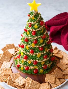 Christmas Tree Cheese Ball made with white cheddar, cream cheese, and covered in parsley, tomatoes, pine nuts and bell peppers.