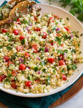 Couscous salad with cucumbers, tomatoes, and herbs shown in a white bowl from the side.