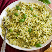 Creamy pesto pasta in a large white serving bowl with a red cloth and fresh basil to the side.