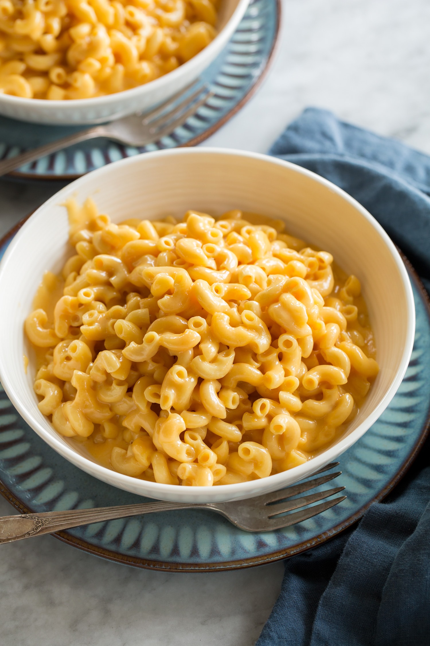 Single serving of crockpot mac and cheese shown in a white soup bowl with a blue plate underneath.