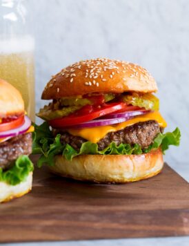 Hamburger shown on homemade bun with lettuce, cheddar, tomatoes and pickles.