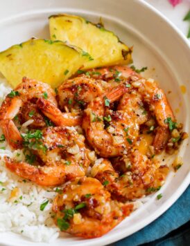 Close up image of Hawaiian garlic shrimp served over white rice with slices of fresh pineapple.