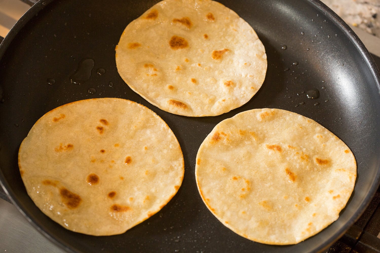 Heating corn tortillas in oil in dark non-stick skillet. 