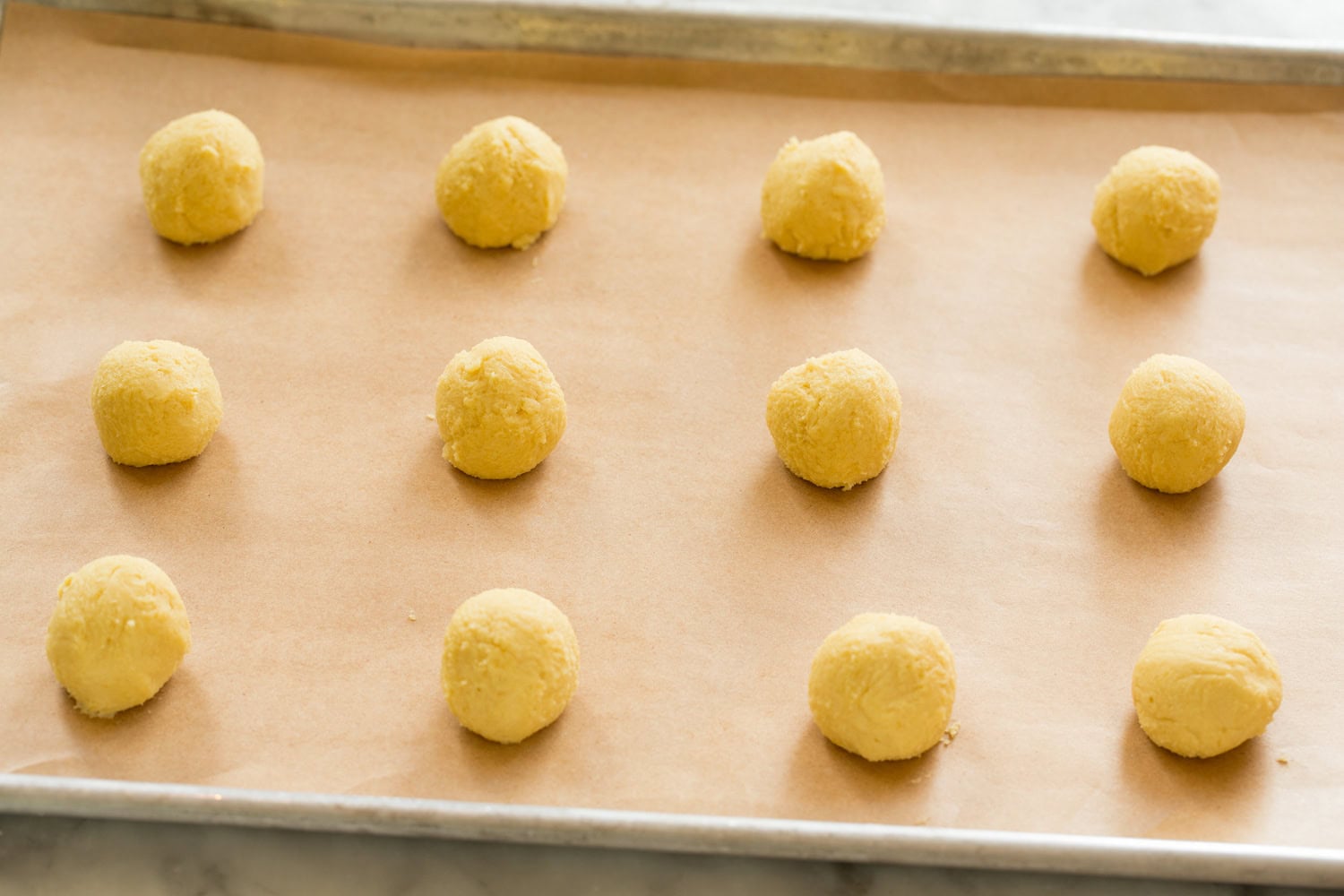 Rolled lemon cookie dough balls on baking sheet.