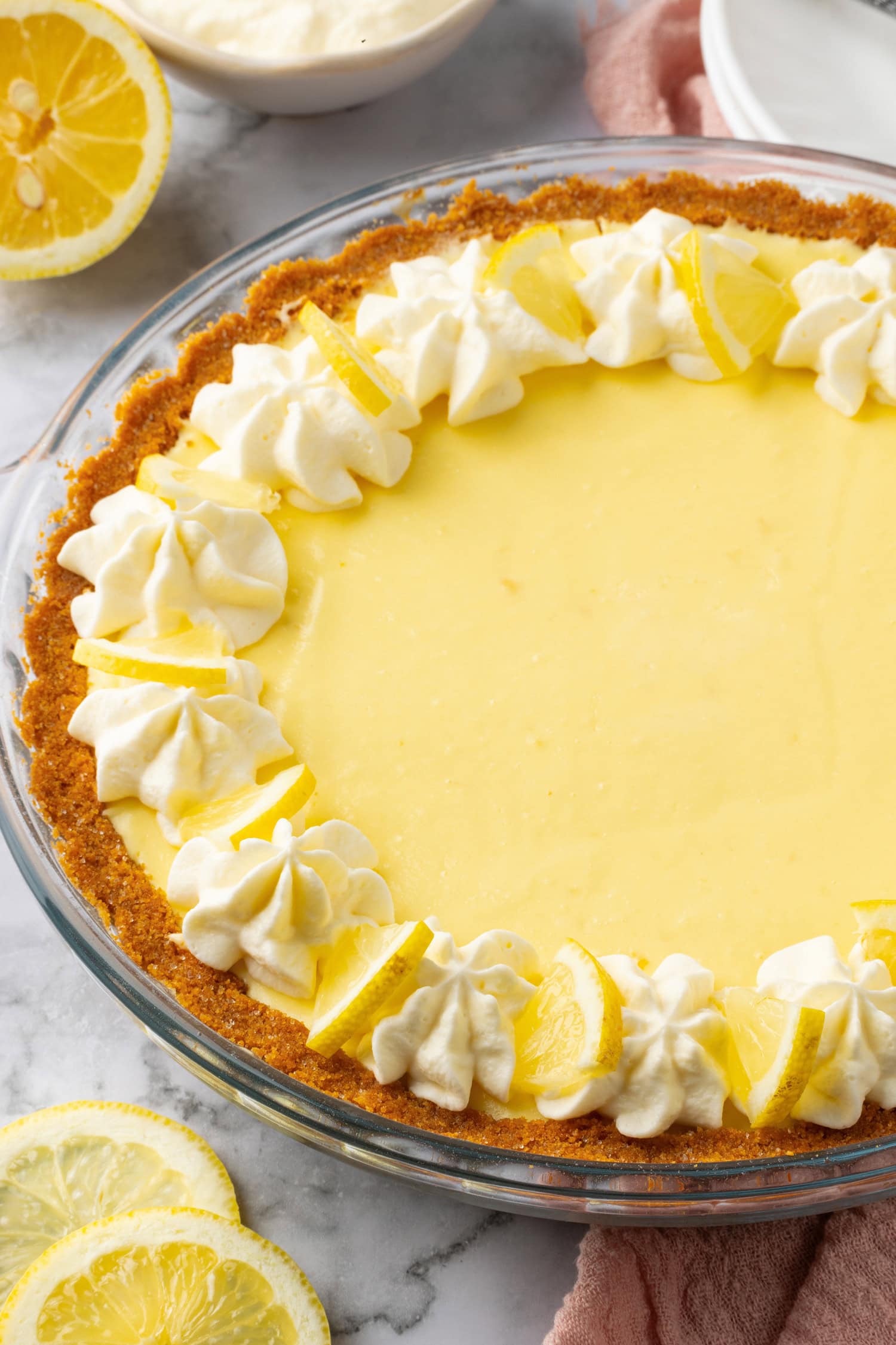 Lemon icebox pie shown from a side angle up close. It's garnished with whipped cream swirls and lemon slices.