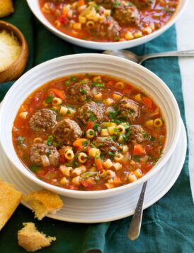 Serving of meatball soup in a white bowl over a white plate with bread to the side.