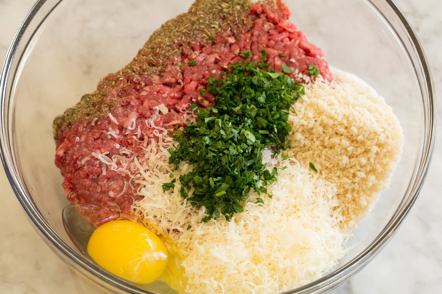 Meatball mixture before mixing in a glass mixing bowl.