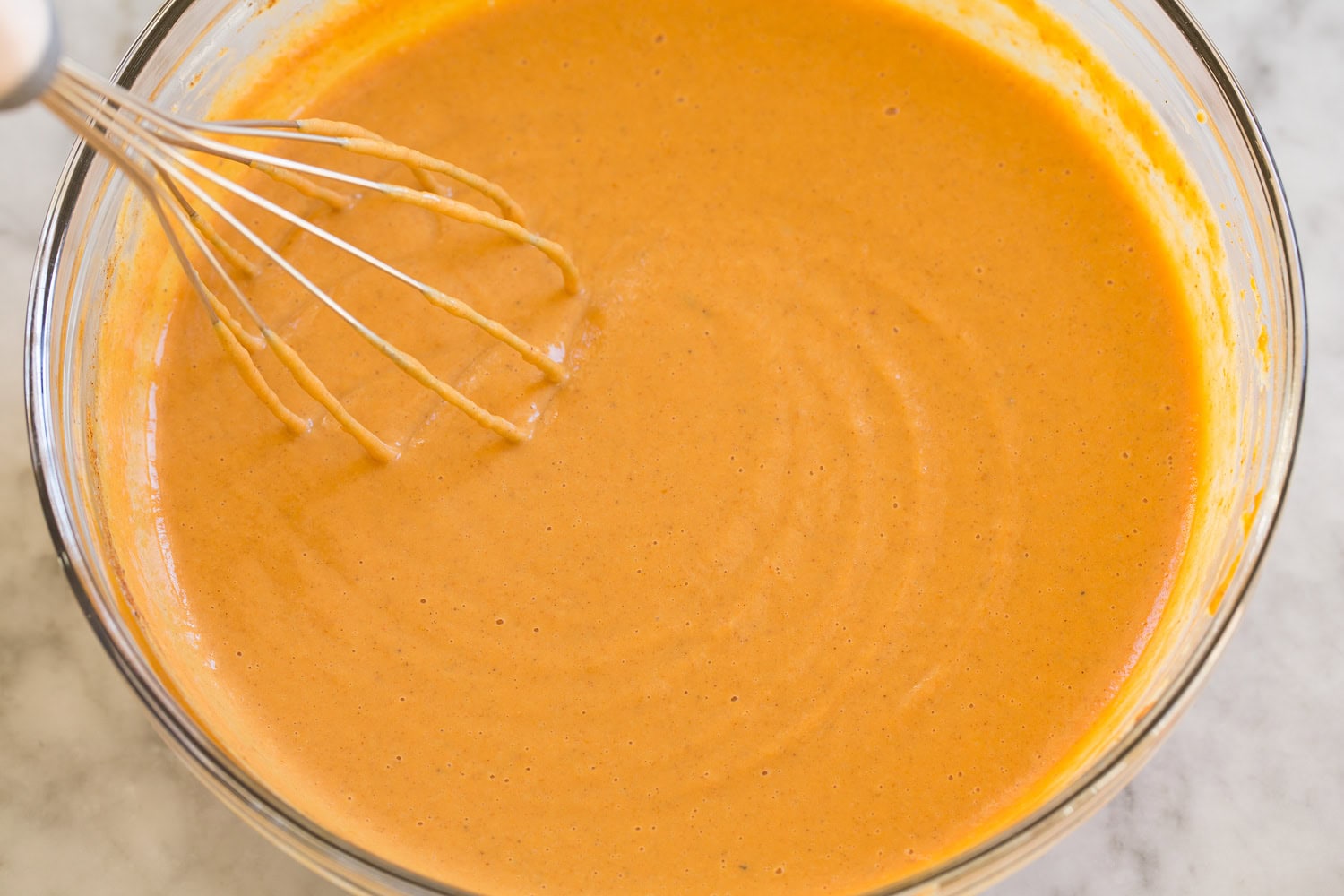 Pumpkin pie filling whisked in a glass mixing bowl.