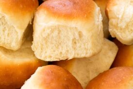 Close up photo of homemade dinner roll showing soft and fluffy texture and golden brown tops.