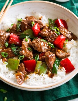 Photo: Pepper Steak in a bowl over white rice. Bowl is resting on a dark green cloth over a marble surface.