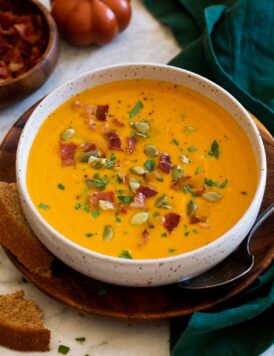 Single serving of pumpkin soup topped with bacon, parsley and pumpkin seeds.