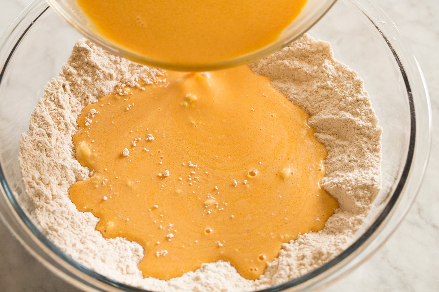 Wet pumpkin mixture added to dry flour mixture in a mixing bowl.