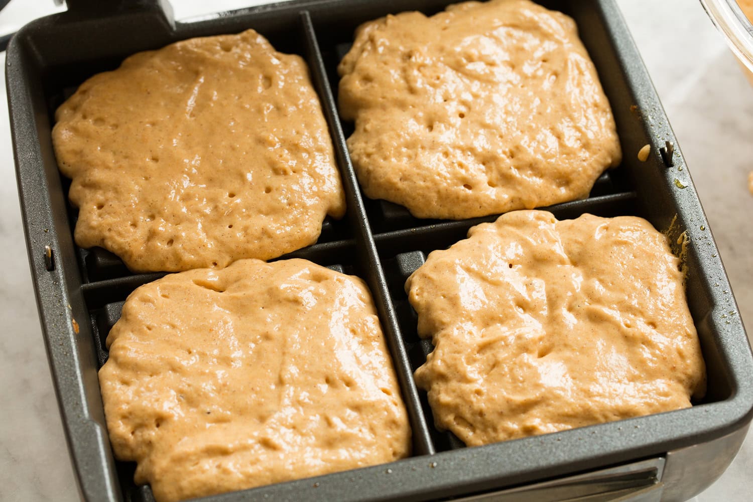 Pumpkin waffle batter shown in waffle iron before cooking.