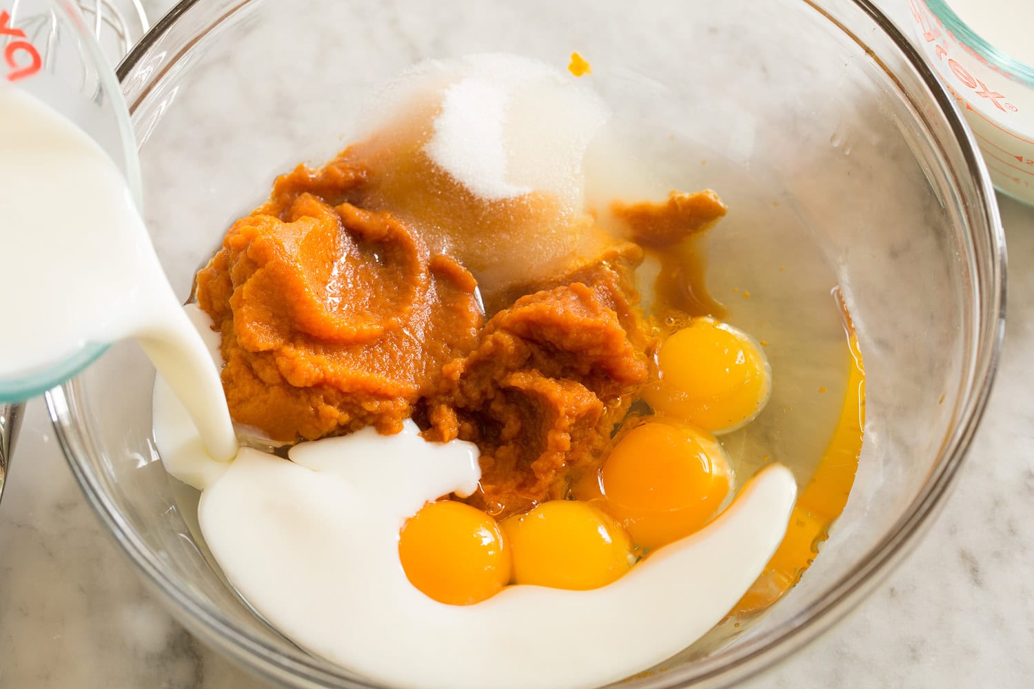 Egg, pumpkin, sugar, milk mixture in a mixing bowl shown before mixed.