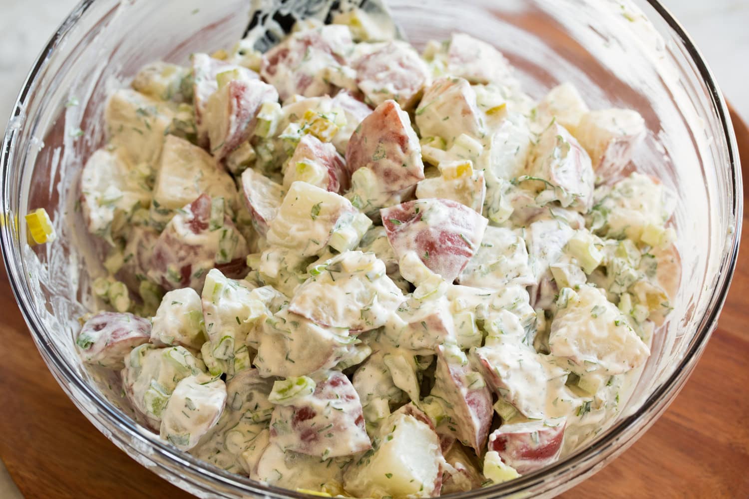 Potatoes tossed with potato salad dressing in glass mixing bowl.