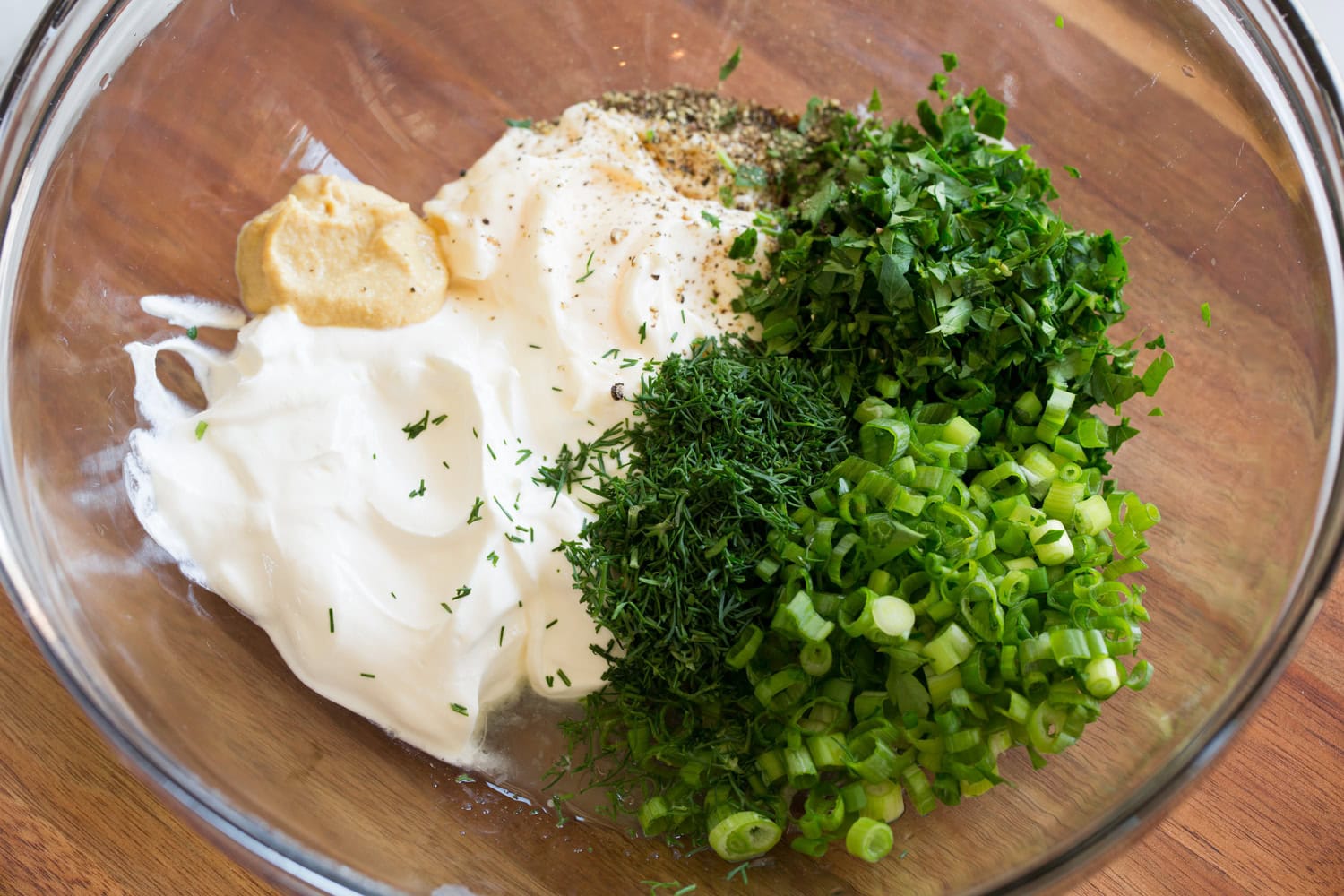 Mayonnaise, sour cream mustard and herbs in a mixing bowl shown before blending.