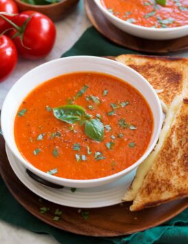 Serving of tomato basil soup shown close up in a white bowl with a grilled cheese to the side.