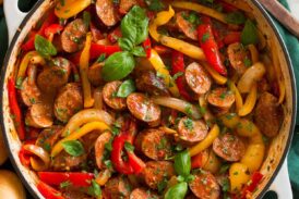 Sliced Italian sausage, peppers and onions in a skillet. Shown with hoagies to the side as a serving suggestion.