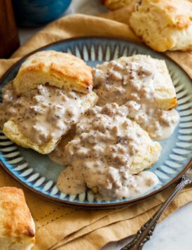 Three buttermilk biscuits with sausage gravy on a blue plate.