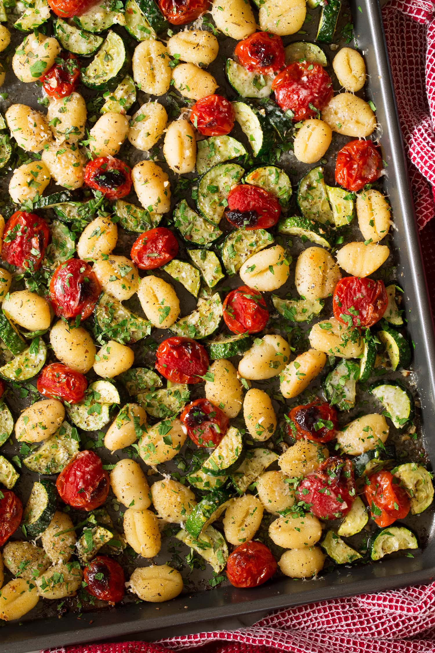 Close up photo of gnocchi on sheet pan with tomatoes and zucchini.