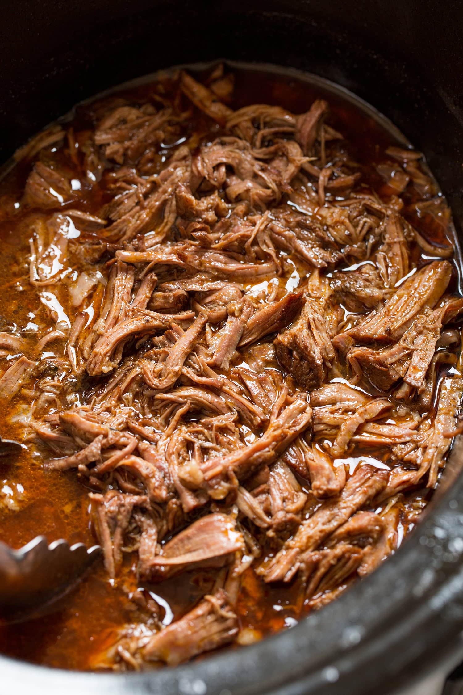 Shredded beef in seasoned broth in the slow cooker.