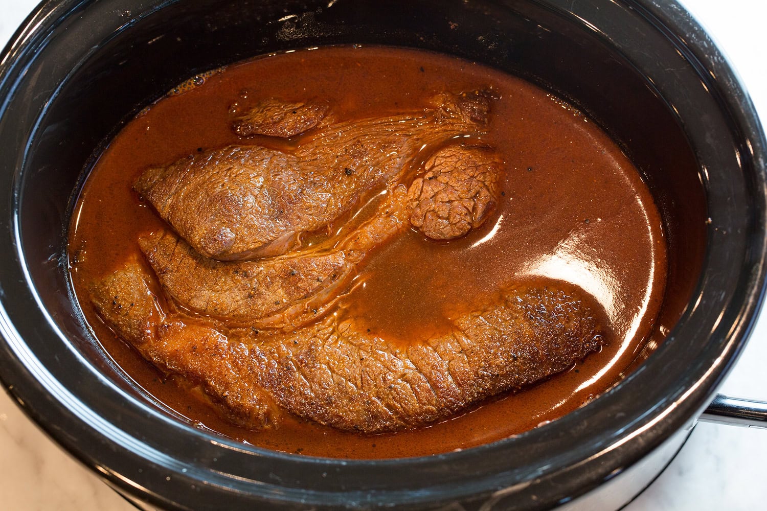 Roast covered in chili seasoned broth in slow cooker.