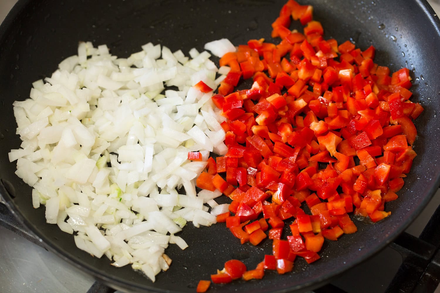 Red bell pepper and yellow onion added to a black skillet.