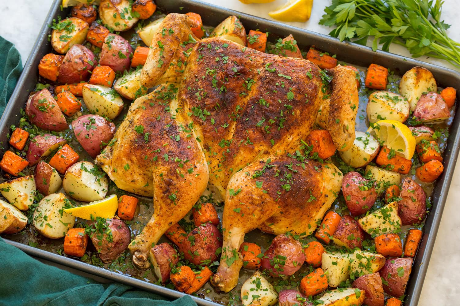 Spatchcock chicken and veggies on baking sheet shown after roasting.