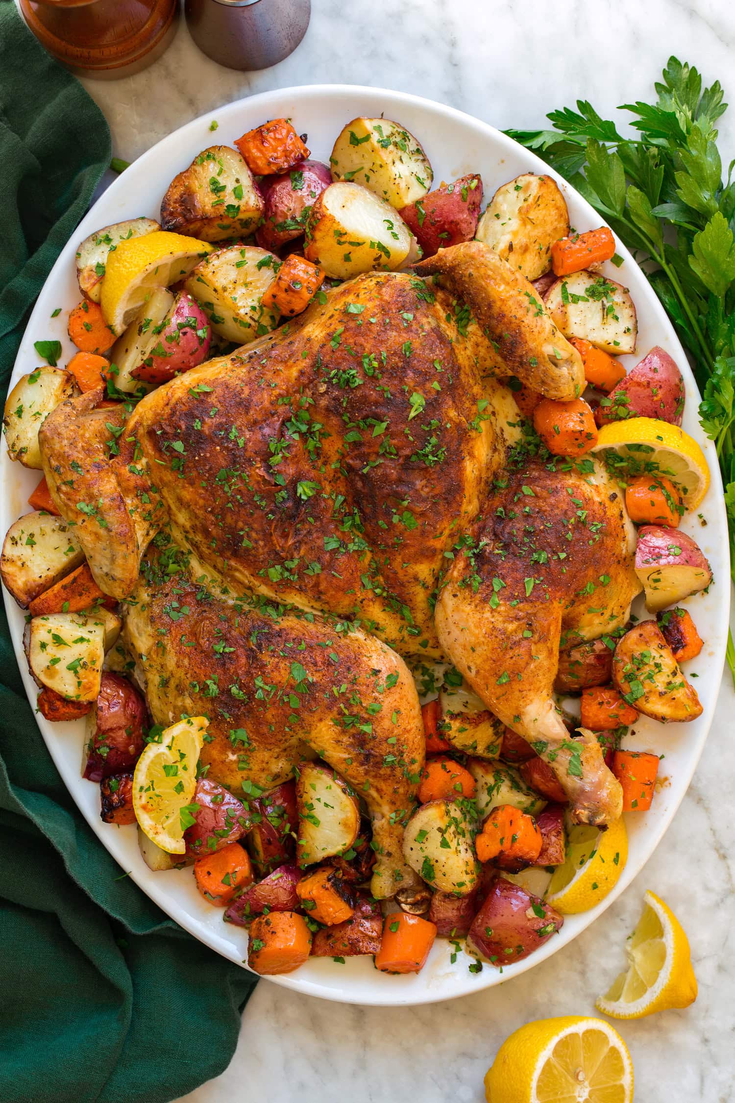 Spatchcock chicken with potatoes and carrots shown on a large oval white serving platter with lemons.